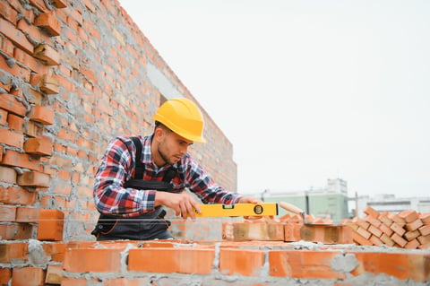 Construction mason worker installing red brick with trowel
