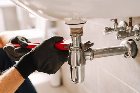 Plumber in black gloves fixes sink pipe with wrench
