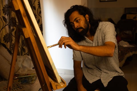 Young Indian man painting on canvas with brush and palette
