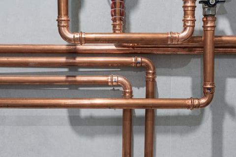 Copper pipes connected with pressed fittings creating industrial pattern on grey tiled wall