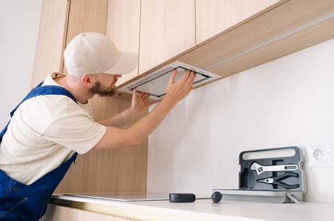 Handyman installing range hood above kitchen cabinet