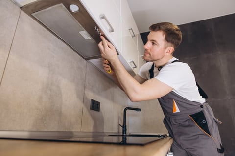 Plumber working in modern kitchen installing range hood