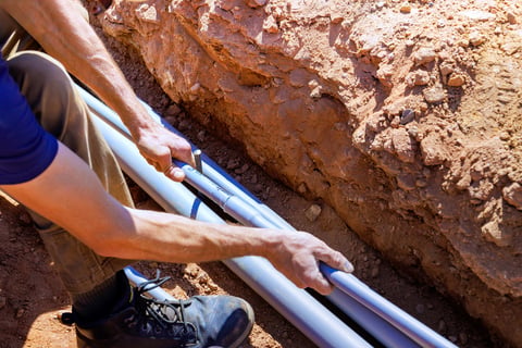 Construction worker positioning plumbing pipes into trench
