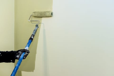 Carpenter paints wall with roller during home renovation