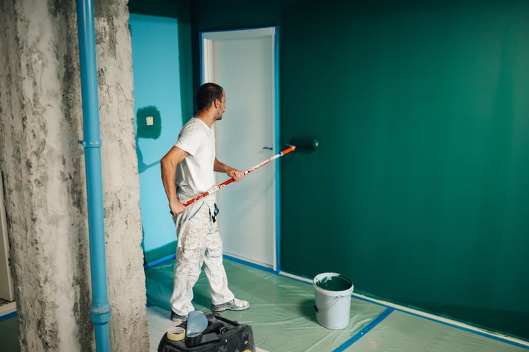 Professional painter using paint roller applying green paint on wall in room