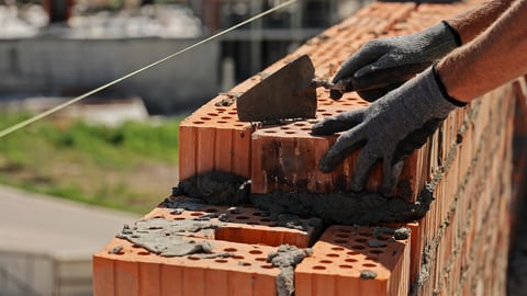 Mason laying bricks with cement mortar using trowel