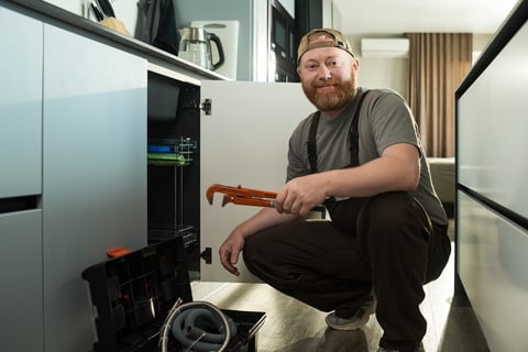 Middle aged handyman kneeling in kitchen holding pipe wrench