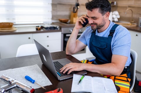 Handyman discussing heating repair on phone while using laptop