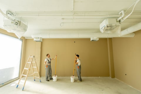 Two painters painting wall beige using long rollers