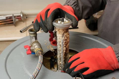 Repairman in red gloves taking damaged heating element with limescale from boiler