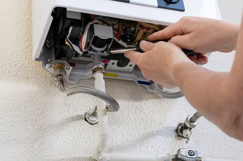 Plumber hands using screwdriver servicing wall-mounted gas water heater