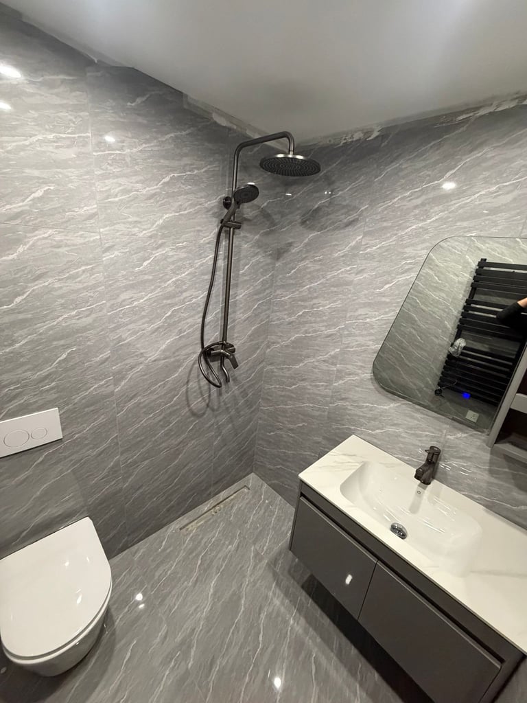 Modern bathroom with gray marble tile walls, white toilet, dark vanity sink, black rainfall showerhead, and towel rack