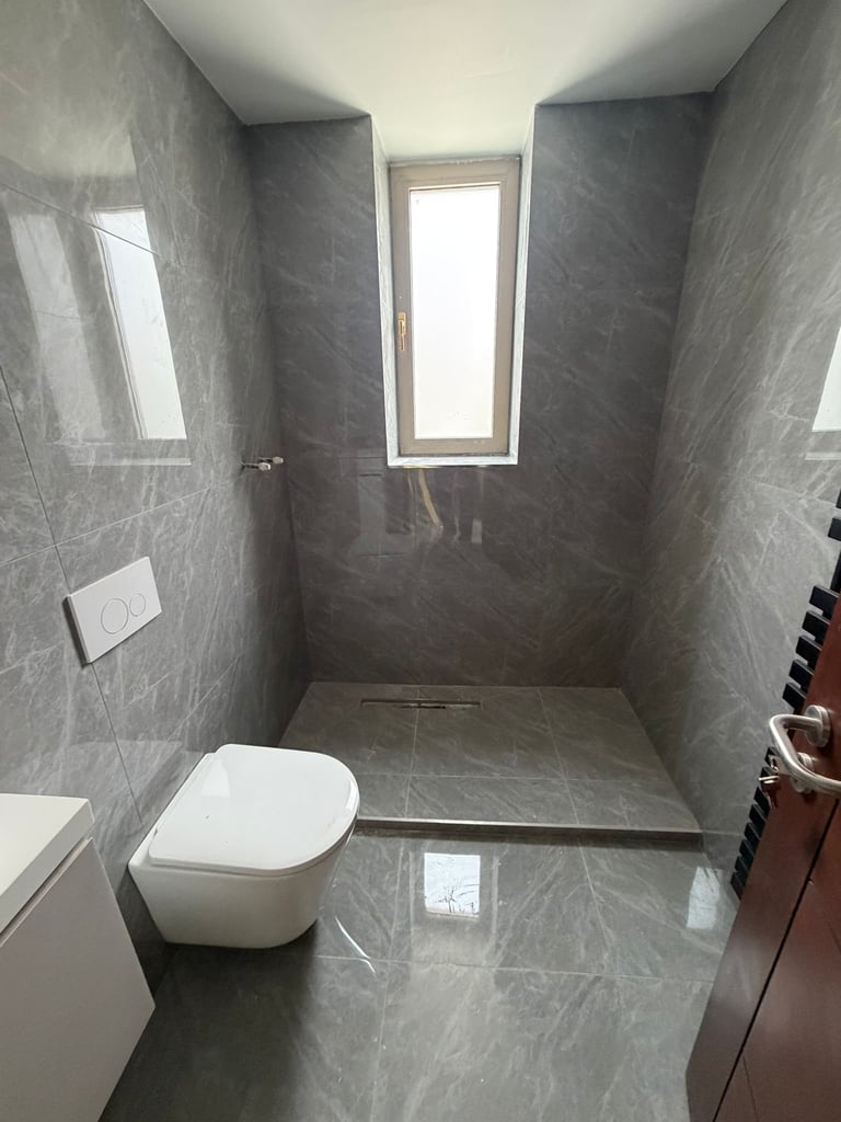 Modern bathroom interior with gray tile walls and floor, white toilet, floor drain, window, and minimalist design