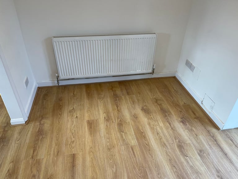 Empty room with laminate wood flooring, white walls, and a white radiator against the wall