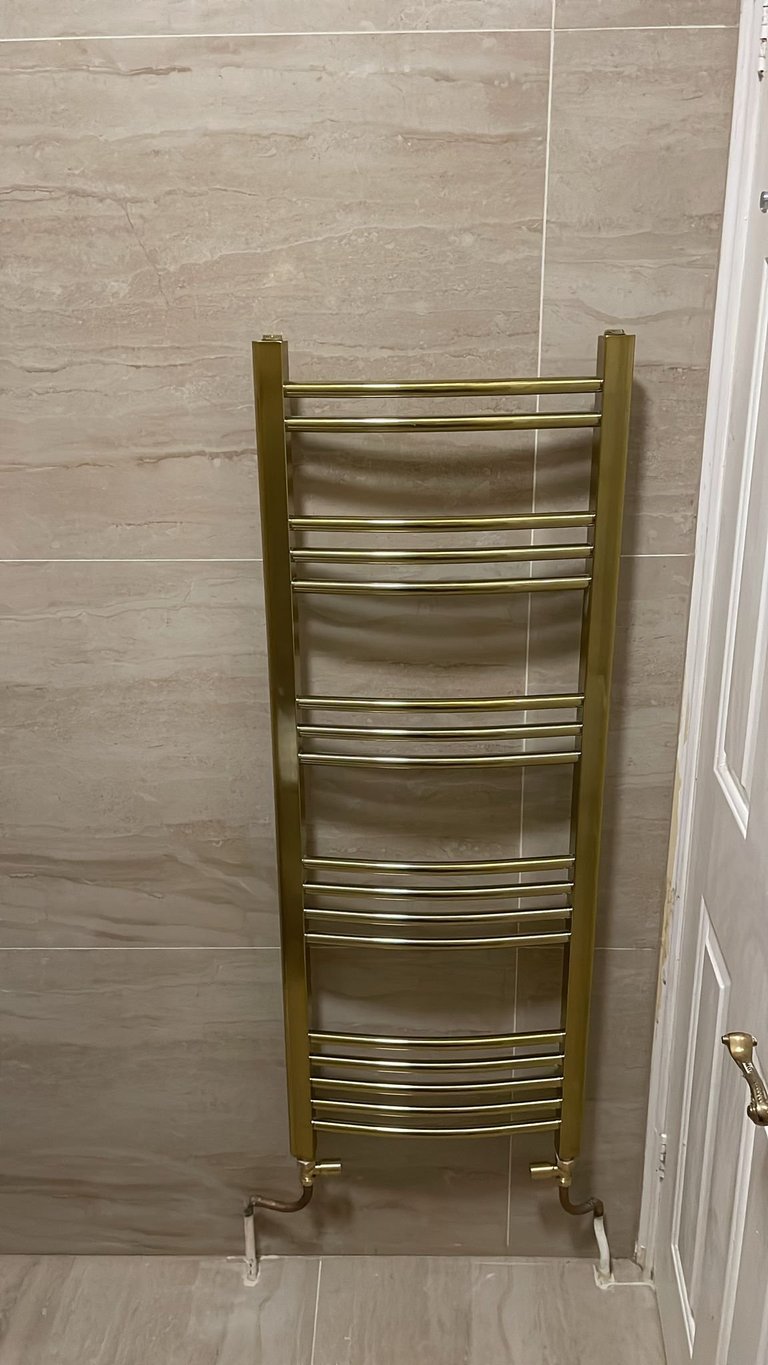 Gold curved towel rack with multiple horizontal bars mounted in a modern tile bathroom