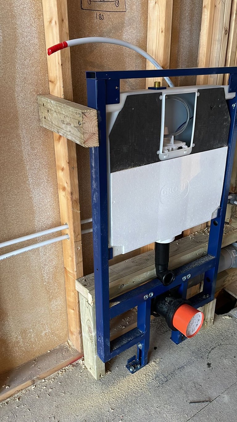 Blue metal frame containing white tank with black covers, mounted on wooden framing in construction setting