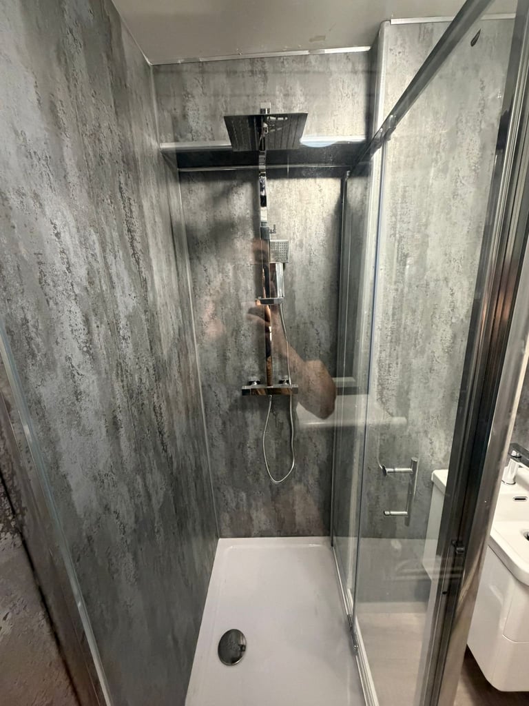 Modern shower stall with dark gray textured tile walls, rainfall showerhead, glass enclosure door, and white base tray