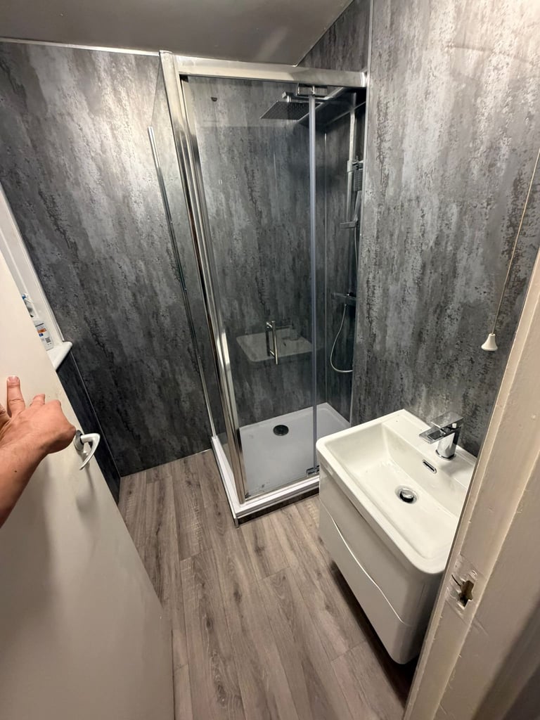 Modern bathroom with walk-in glass shower enclosure, white vanity sink, and dark gray tile walls