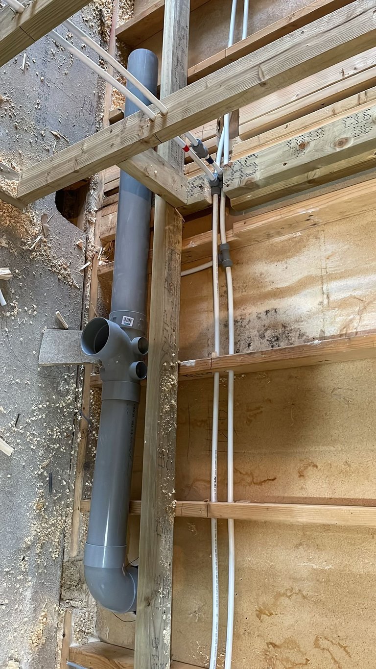 Construction framing showing PVC pipe with elbows mounted on concrete wall and wooden beams during building installation