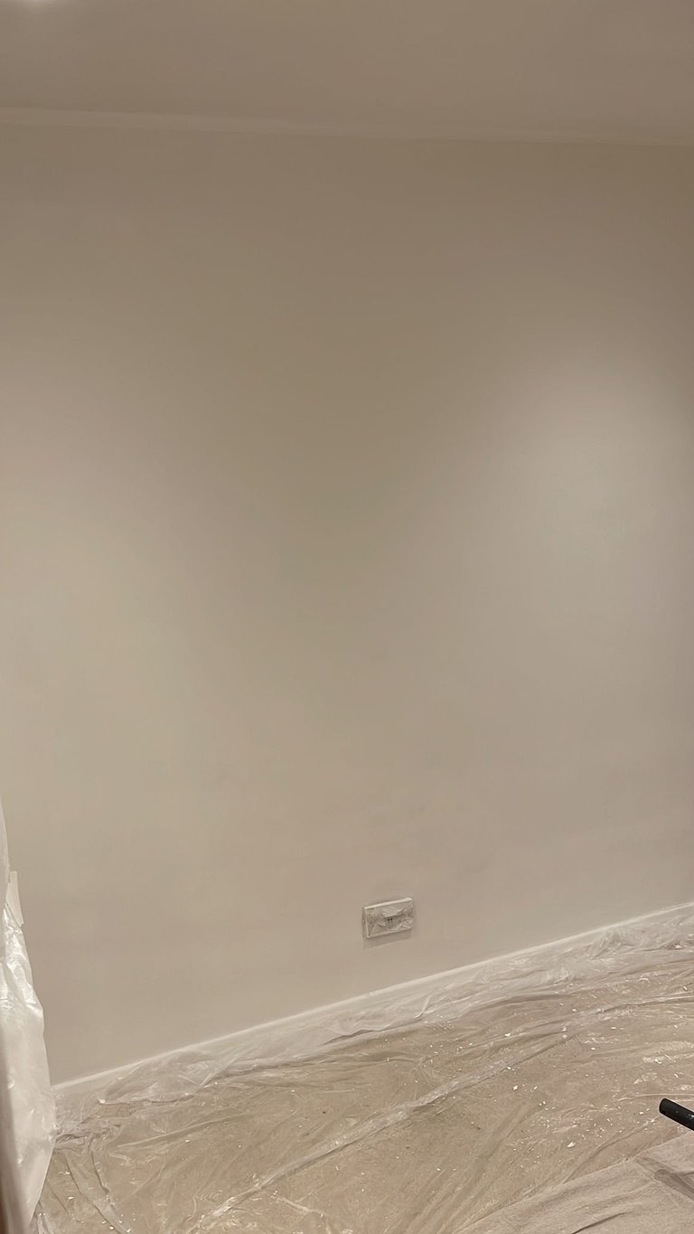 Beige drywall with small electrical outlet box mounted in center, clear plastic sheeting on floor below