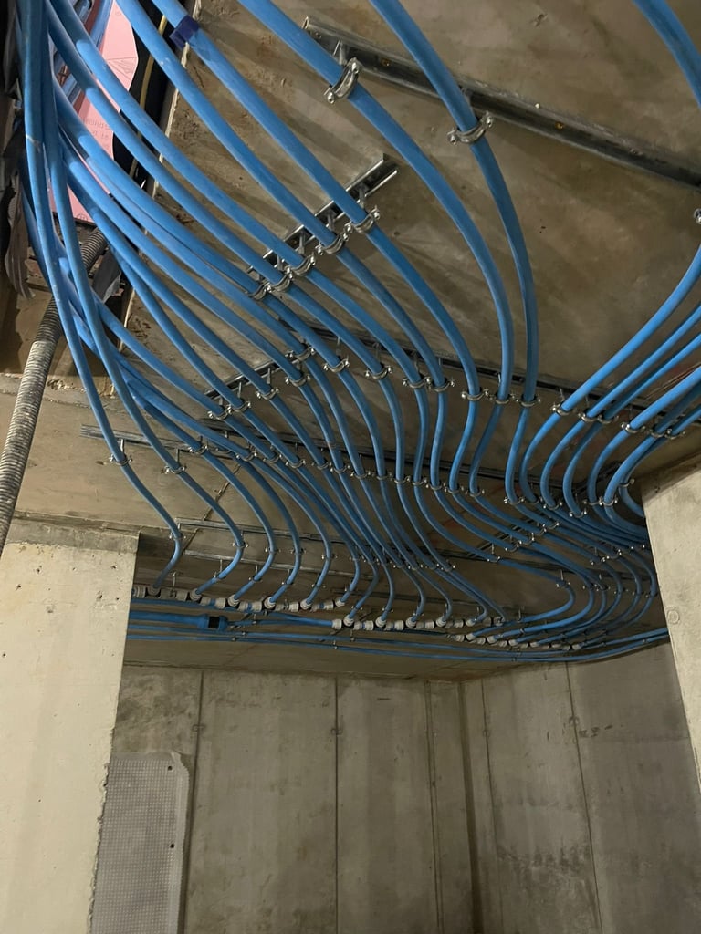 Blue electrical conduit and cables organized in parallel runs mounted on ceiling with metal clamps and junction boxes