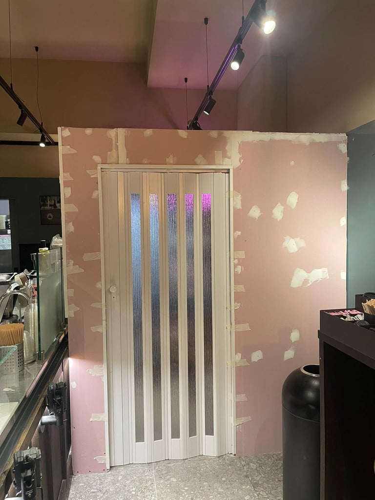 Interior room with white accordion door surrounded by pink drywall patches and track lighting overhead
