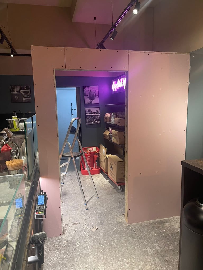 Pink drywall room under construction with purple neon sign, ladder, and storage boxes inside