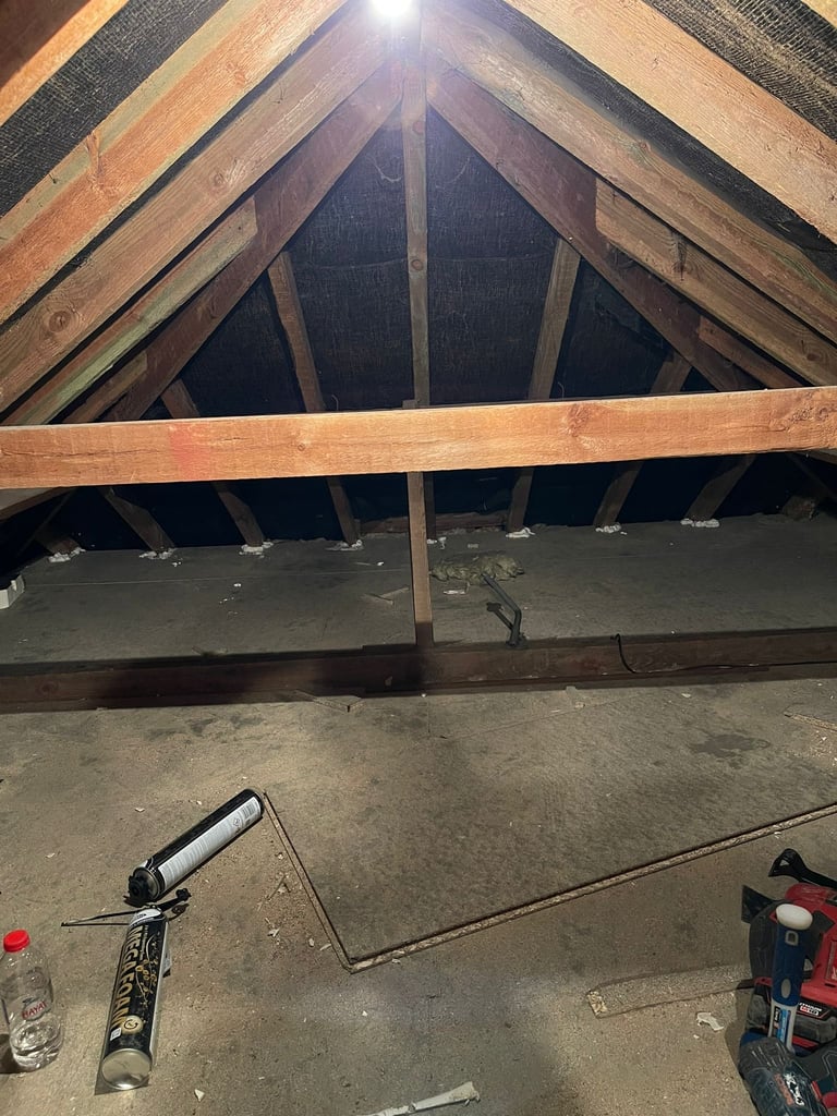 Interior view of attic space with wooden roof beams, concrete floor, and construction tools including a caulking gun and power drill