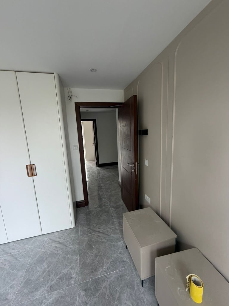 Modern hallway interior with gray tile flooring, white walls, white closet door, dark wooden door frame, and storage furniture