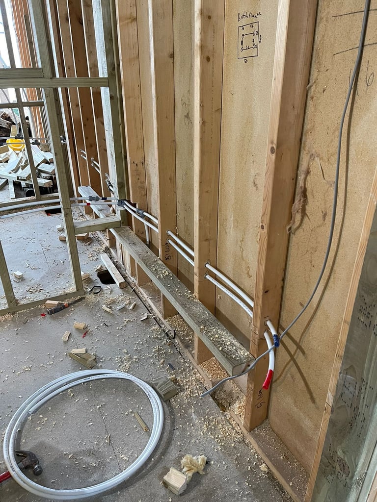 Construction site interior showing wooden wall framing, electrical wiring, metal studs, and plastic bucket on concrete floor