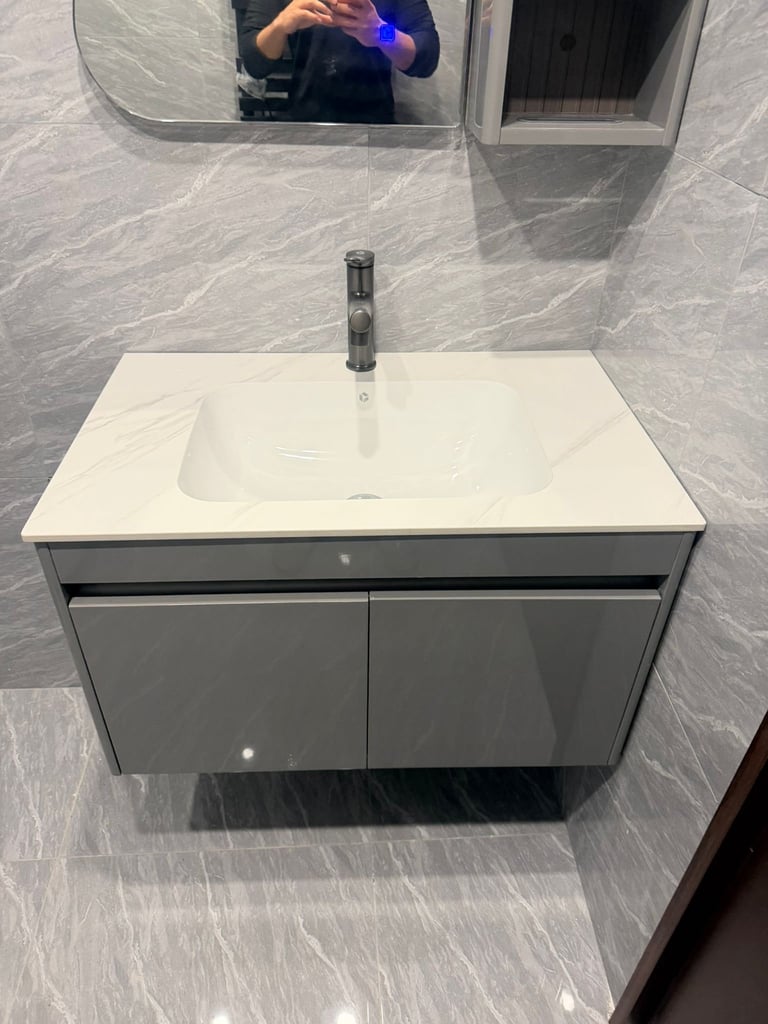 Modern gray bathroom vanity with white sink and chrome faucet mounted on gray tile wall with mirror above