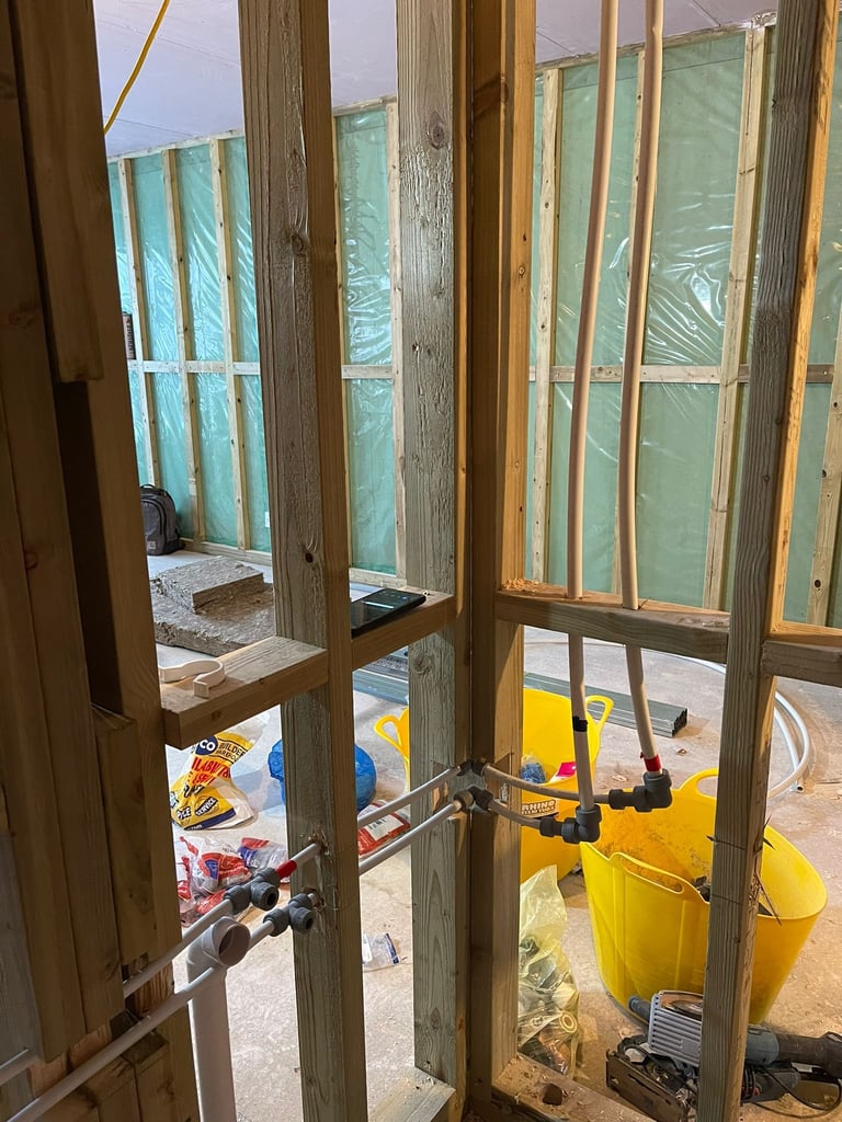 Construction site viewed through wooden window frames with glass and plastic coverings, yellow equipment visible inside