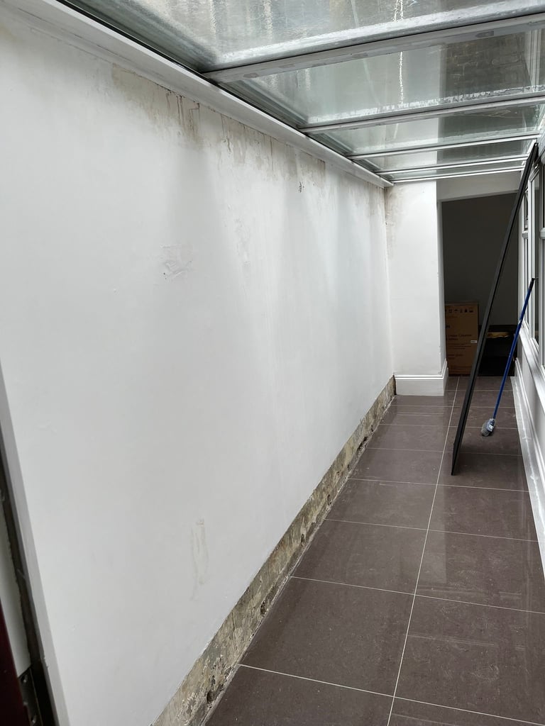 Empty hallway with white walls, dark tile flooring, and glass ceiling panels overhead