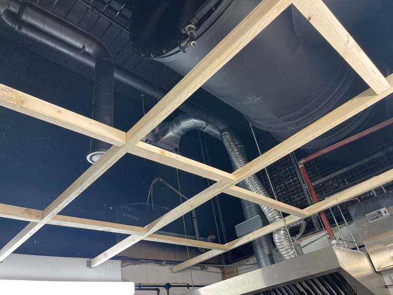Modern ceiling design with geometric white beams intersecting across dark blue background with industrial lighting and ductwork visible