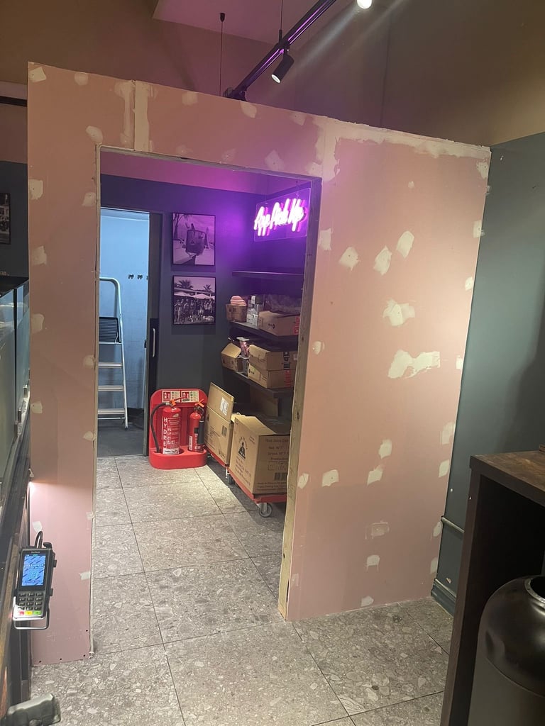 A doorway with pink drywall framing leading to a room with a purple neon HAHA sign and red mailbox inside