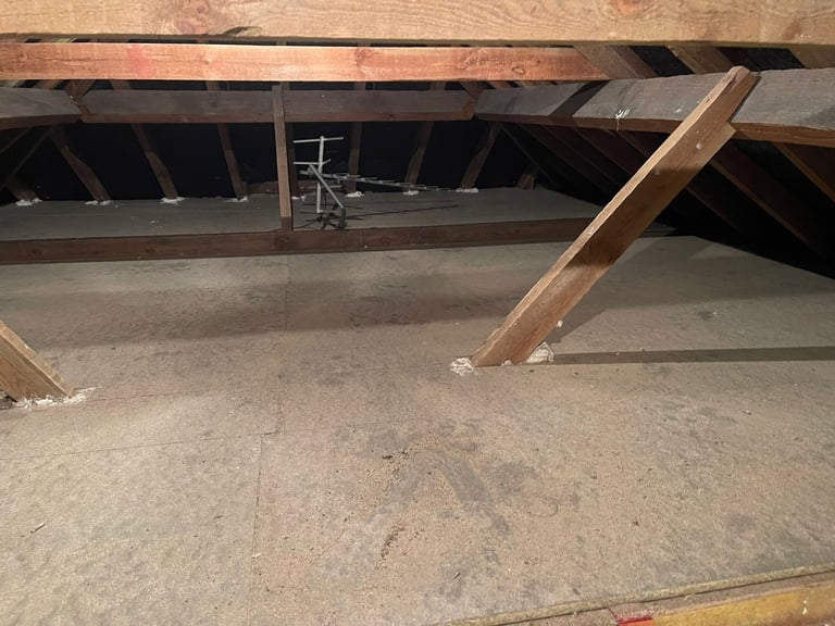 Interior view of crawlspace under building with concrete floor, wooden support posts, and metal ductwork visible
