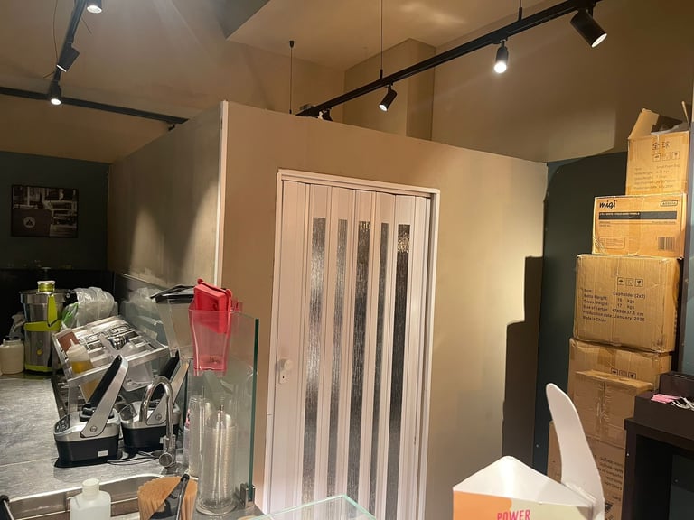 Interior of a storage or utility room with cardboard boxes, track lighting, a white accordion door, and shelving with items