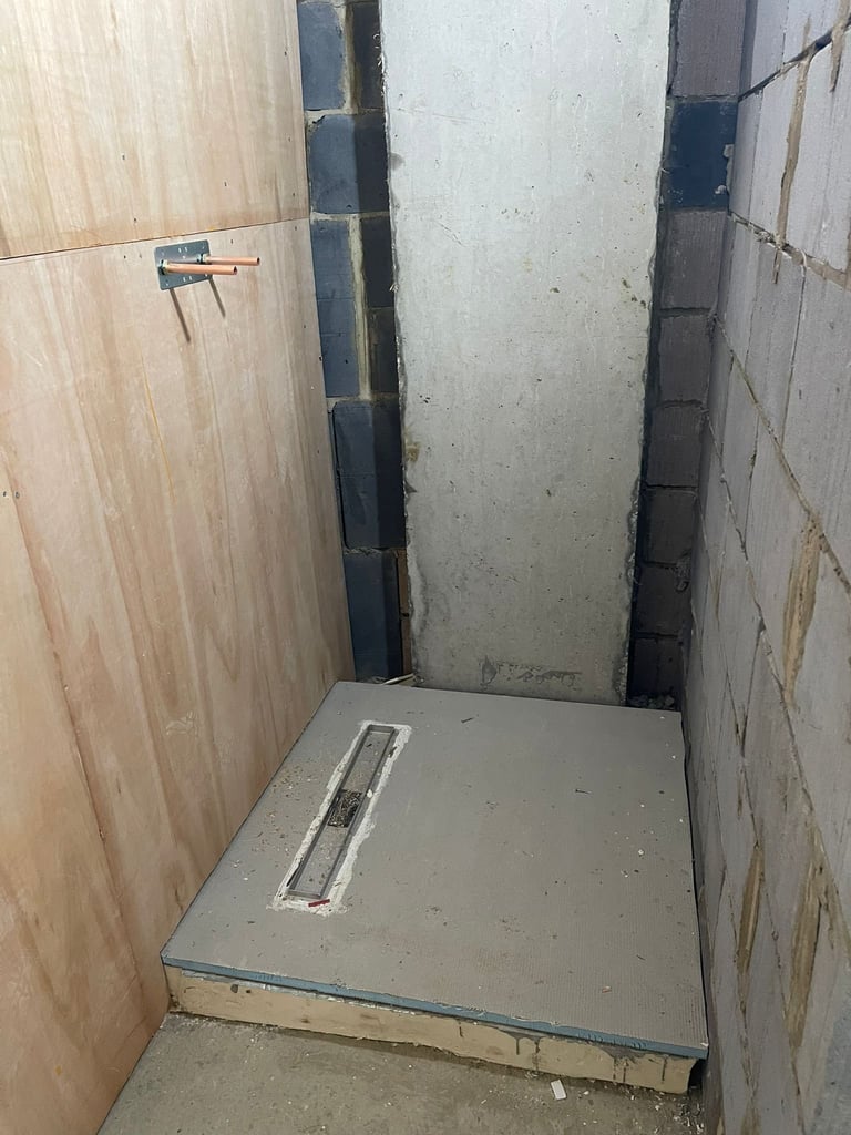 Unfinished bathroom shower alcove with concrete floor, tiled walls, and drainage grate, under construction