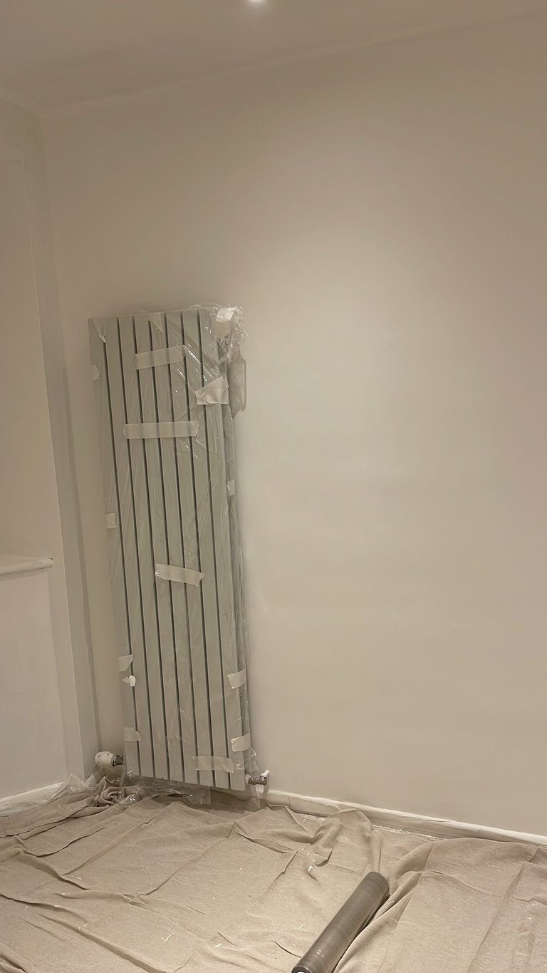 White vertical radiator wrapped in plastic on a white wall with drop cloth covering the floor during installation or renovation