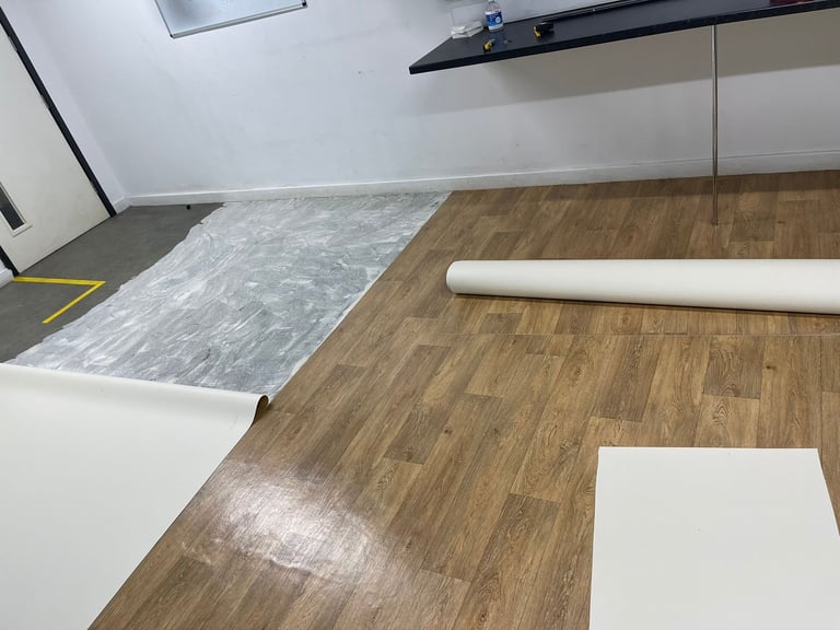 Flooring samples displayed on wooden floor showing vinyl plank patterns and roll materials