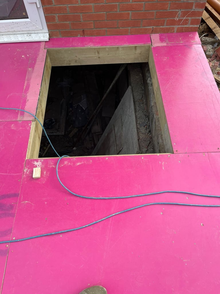 Open square hole in bright pink floor with electrical cable running across, red brick wall visible above