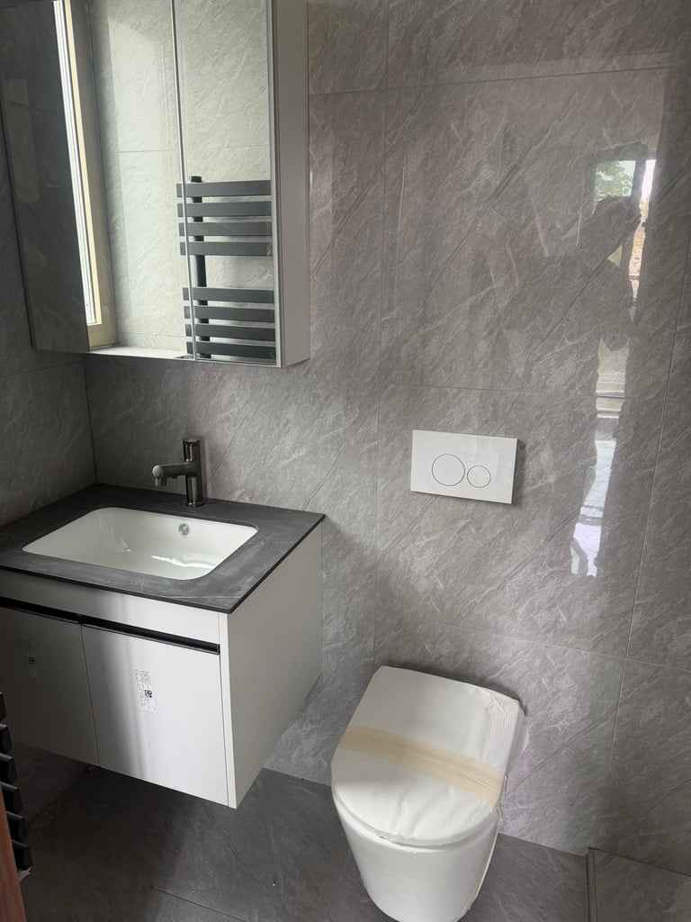 Modern gray tile bathroom with white sink vanity, toilet, heated towel rack, and mirror with lighting