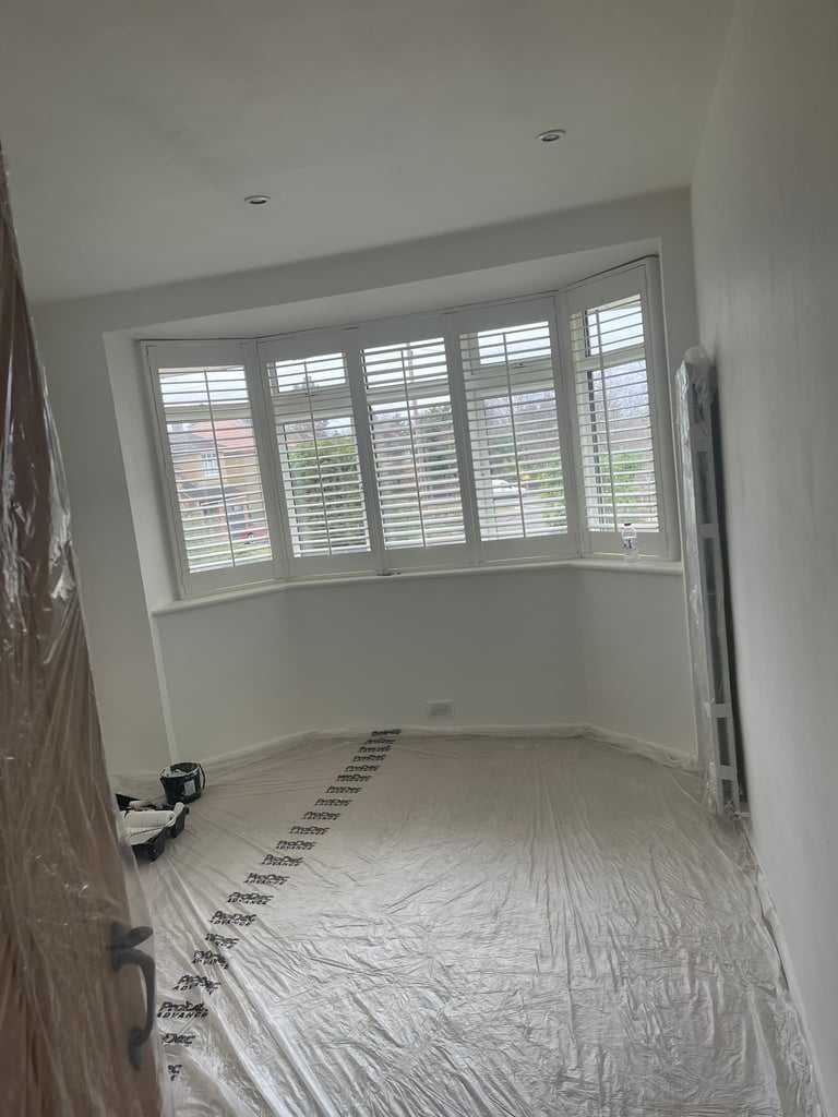 Empty room under construction with white shuttered window, plastic floor covering, and ceiling fixtures