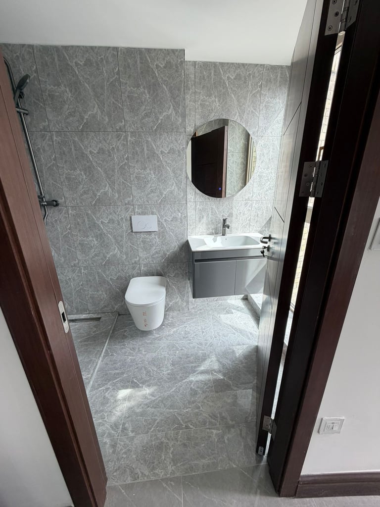Modern bathroom with gray marble tiles, white toilet, white sink with mirror, and dark brown doors