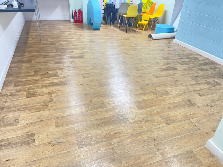 Spacious room with light wood laminate flooring, yellow chairs, blue storage containers, and white walls with blue accent trim