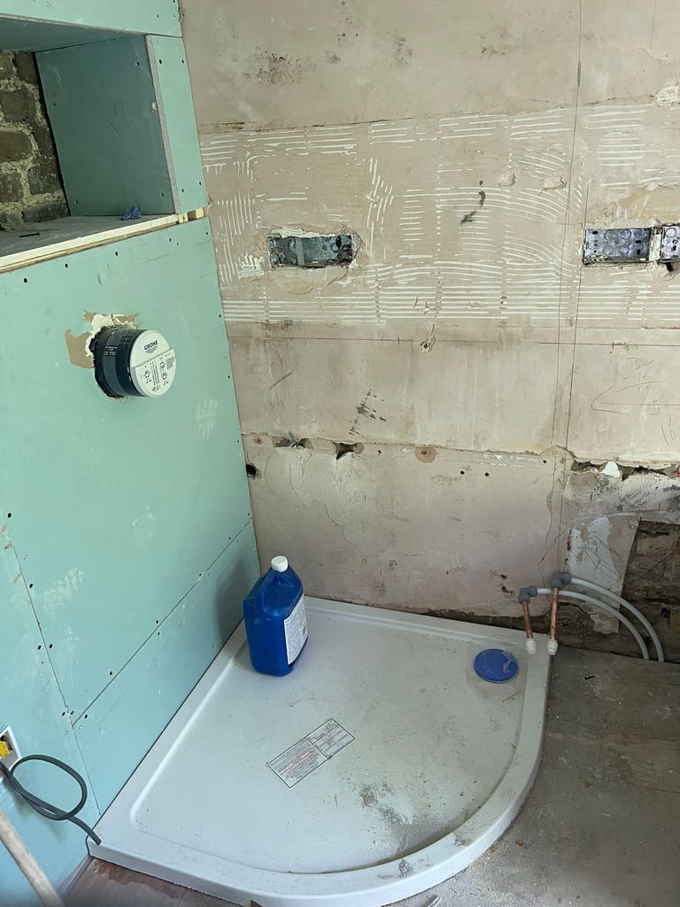 Unfinished bathroom under construction with turquoise drywall, white curved shower base, blue detergent bottles, and exposed electrical outlets