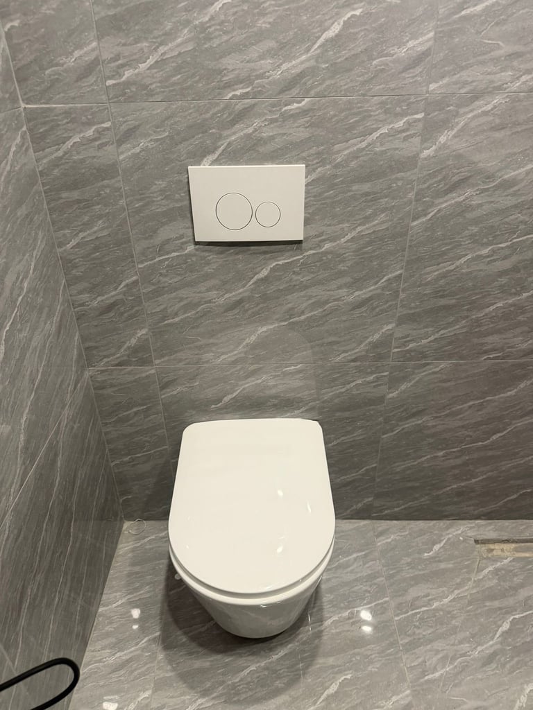 Modern white toilet with closed lid in a gray marble-tiled bathroom with a two-button wall-mounted flush plate