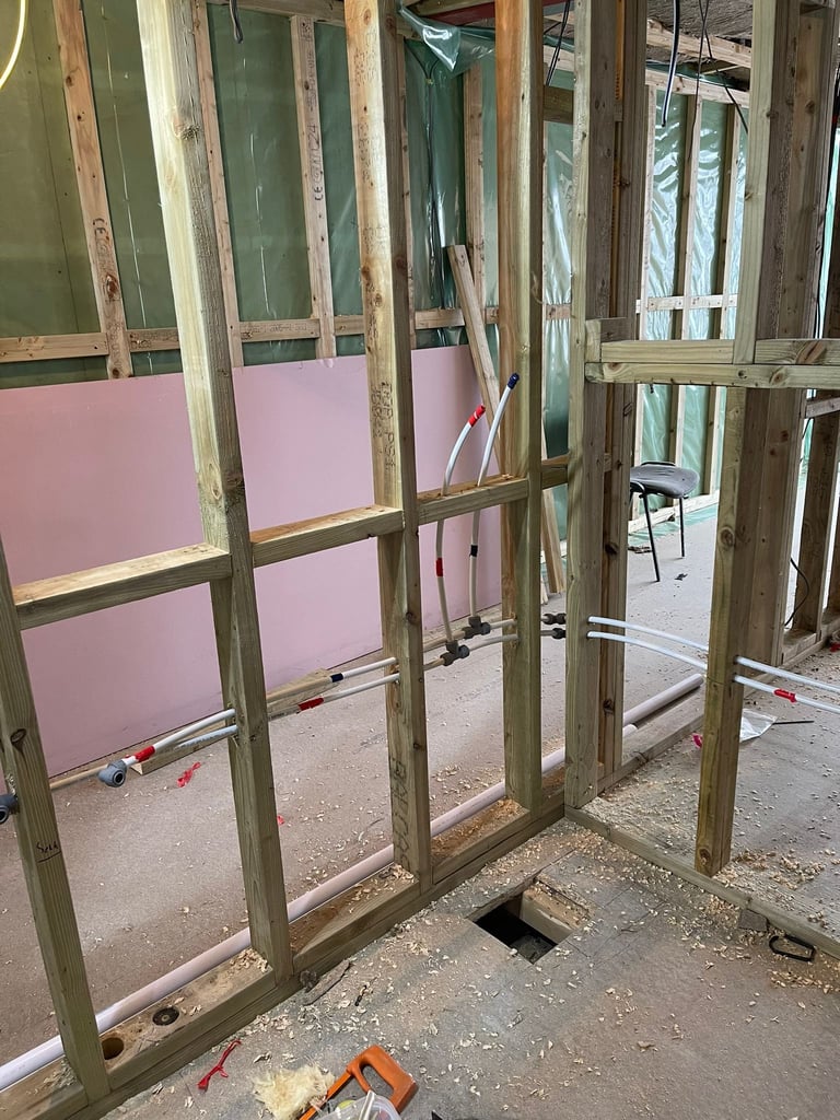 Interior construction site with wooden framing, pink drywall sheets, and exposed studs in an unfinished room