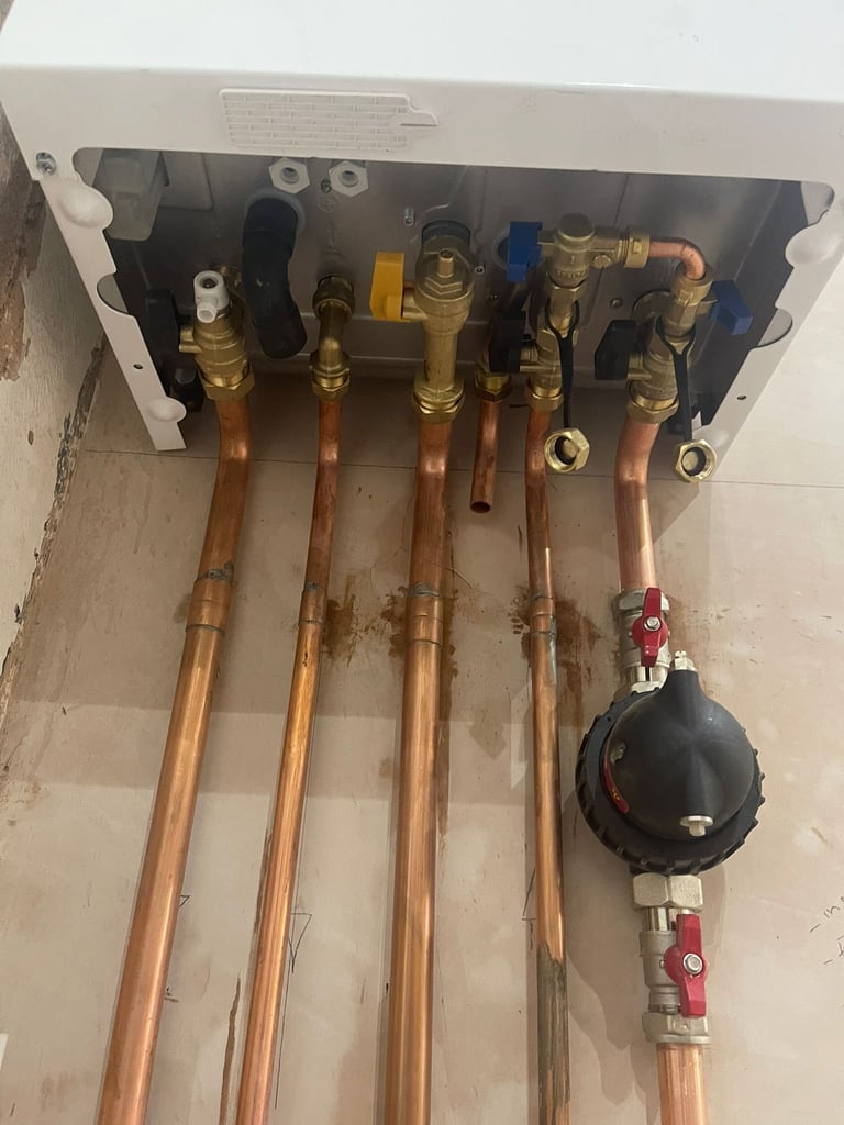 Plumbing manifold with copper pipes and brass valves, mounted on wall with shut-off valve visible at bottom right