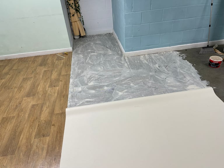 Interior room under renovation with wood flooring, plastic floor covering, and blue-painted walls with white trim